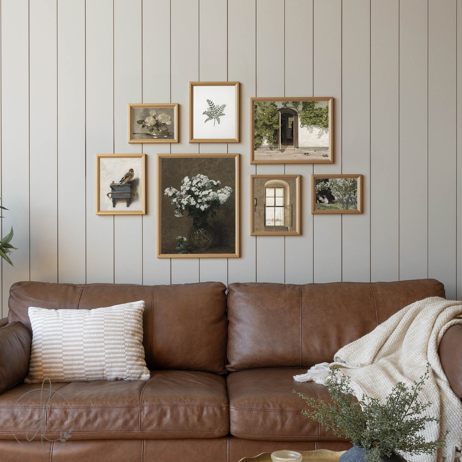 Brown leather sofa with decorative pillows and a blanket against a wall with framed botanical prints.