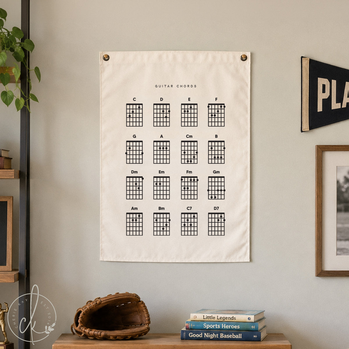 A rectangular off-white fabric wall hanging featuring a black printed grid of guitar chords. The chart displays sixteen distinct chord diagrams labeled with letters and symbols, including C, D, E, F, G, A, Cm, B, Dm, Em, Fm, Gm, Am, Bm, C7, and D7.