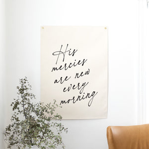 Poster with 'His mercies are new every morning' text on a wall with a plant and chair.