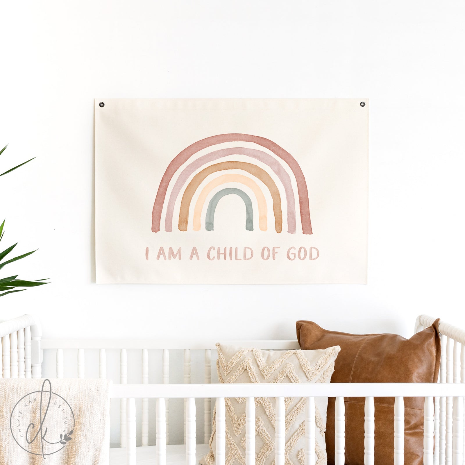 Decorative wall hanging with rainbow and 'I am a Child of God' text above a crib.