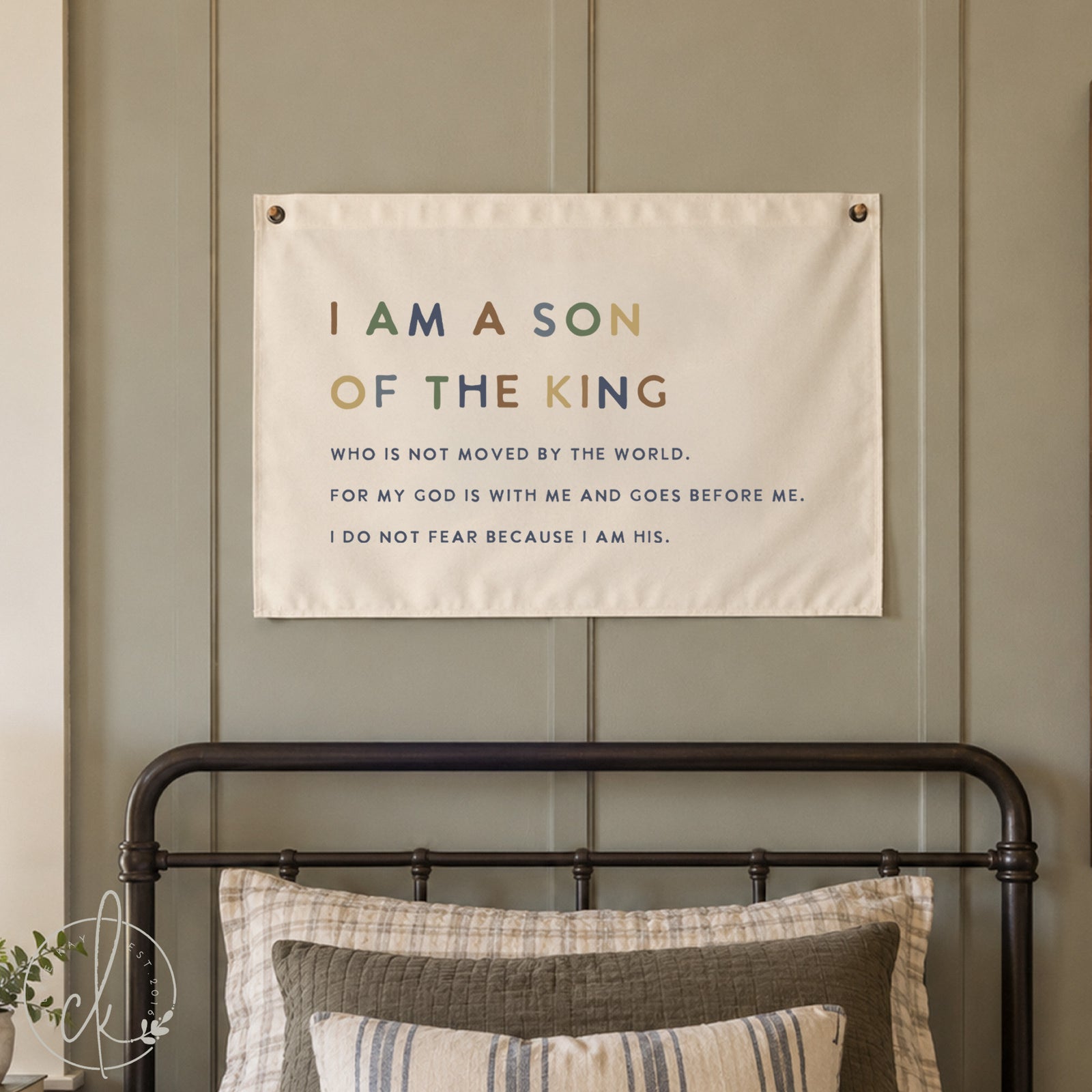 A rectangular off-white fabric wall hanging featuring the text I AM A SON OF THE KING WHO IS NOT MOVED BY THE WORLD. FOR MY GOD IS WITH ME AND GOES BEFORE ME. I DO NOT FEAR BECAUSE I AM HIS. The text uses varied colors.
