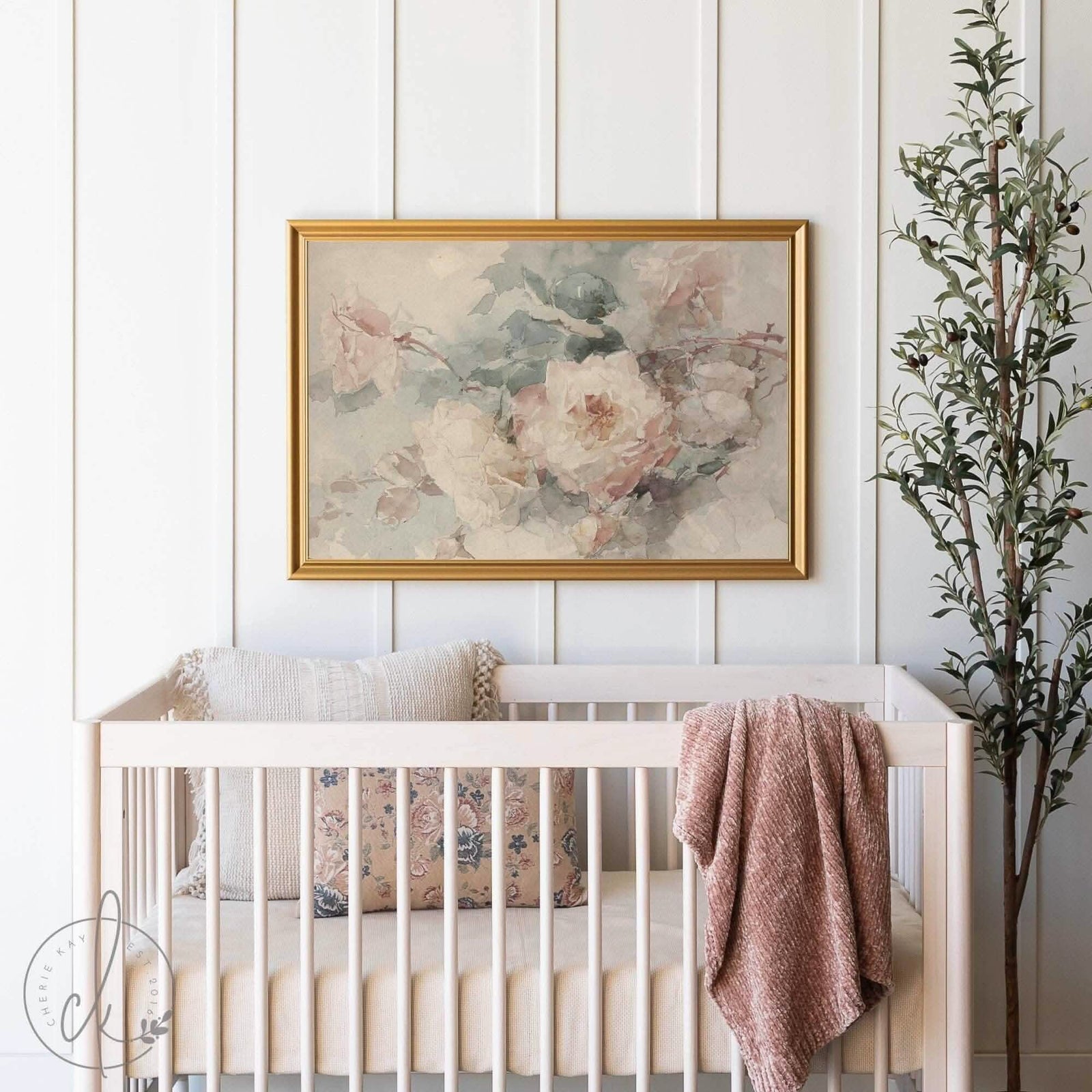 A vintage-style nursery featuring a wood crib with pillows and a blanket draped over the side. Above the crib hangs a framed watercolor painting of pink and white roses, adding a touch of elegance to the room.