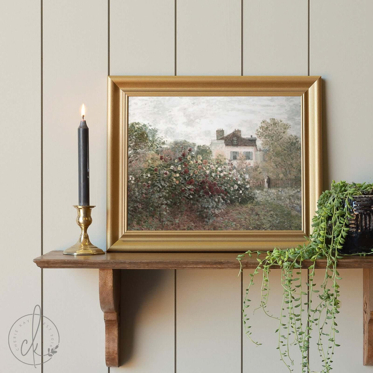 Small gold-framed impressionist landscape painting showcasing a cottage garden in full bloom, displayed on a wooden shelf with a brass candleholder. Perfect for vintage-inspired home décor and available in multiple sizes.