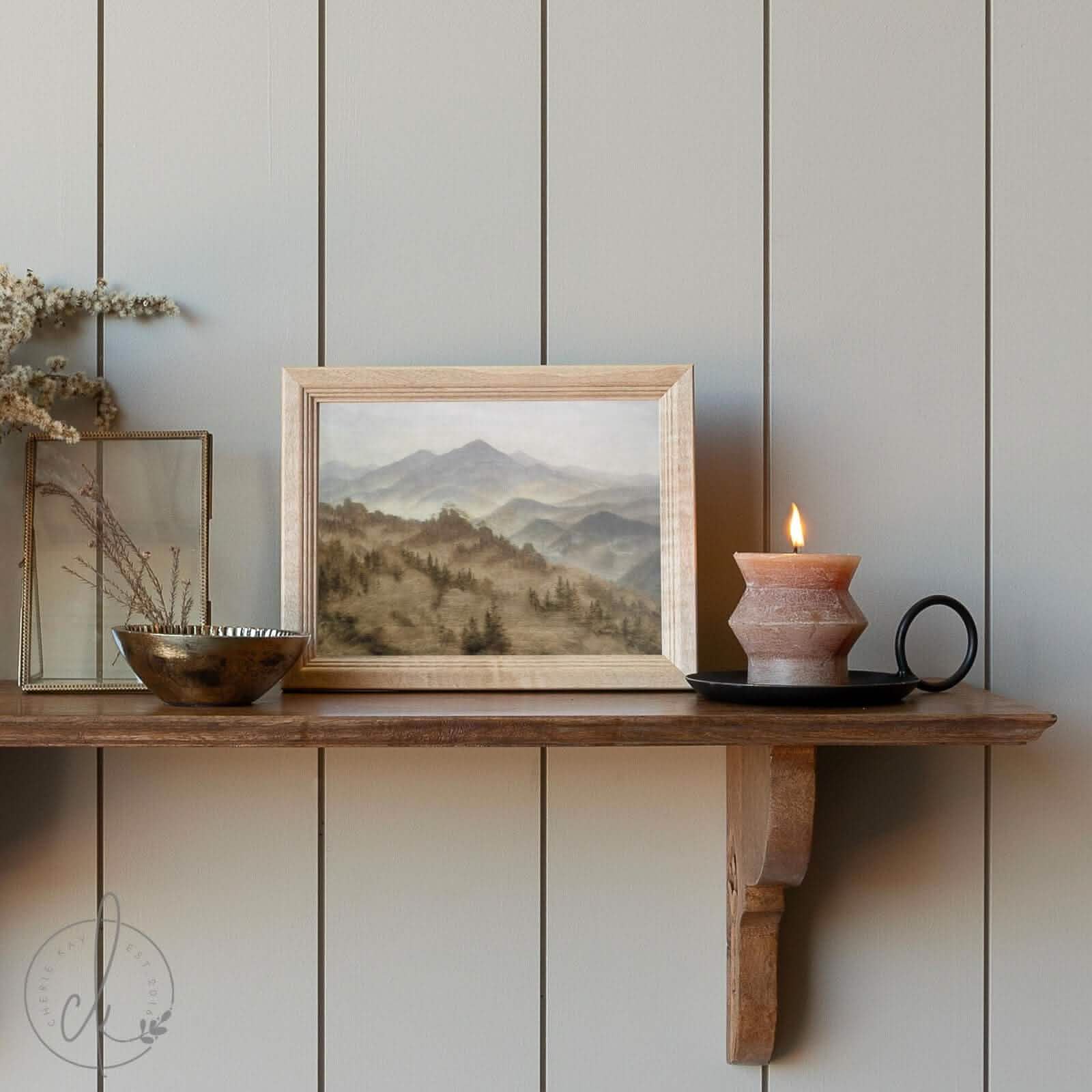 Small wooden-framed mountain landscape painting showcasing misty rolling hills, elegantly displayed on a rustic shelf with a warm candle. Ideal for adding a serene, nature-inspired accent to your décor and available in multiple sizes