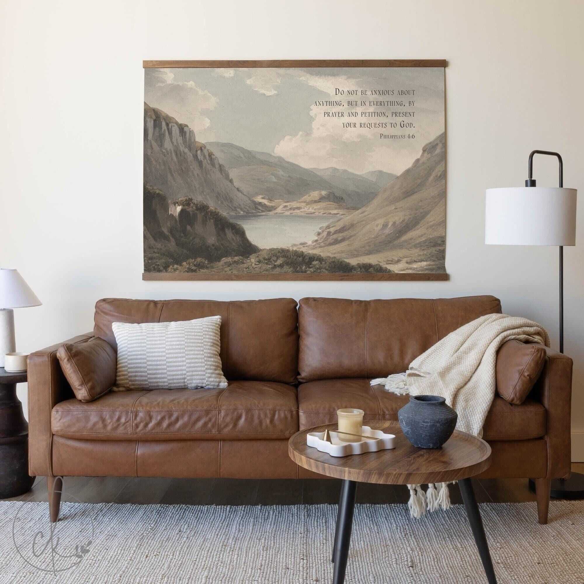 A cozy living room with a brown leather sofa, a wooden coffee table, and a wall-mounted landscape art piece featuring scripture. A light rug, lamps, and decorative accents complete the space.