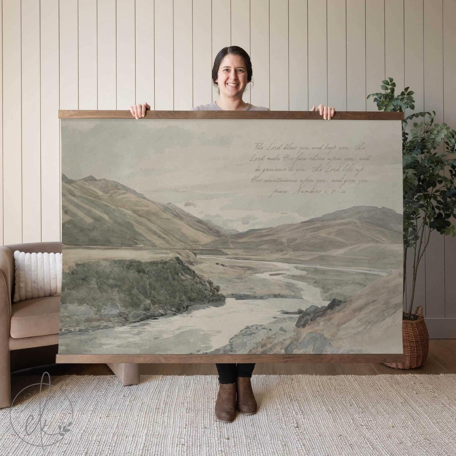 Oversized vintage-style framed wall tapestry featuring a muted mountain and river landscape with handwritten scripture from Numbers 6:24–26. Held by a person to show scale. Available in multiple sizes and frame options.