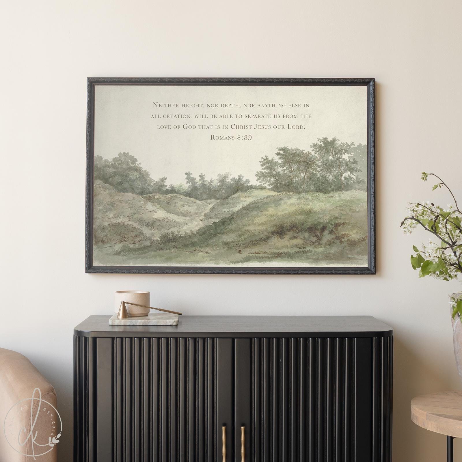 Framed vintage landscape art with Romans 8:39 Bible verse, featuring a peaceful green hillside and trees, styled above a modern black cabinet in a neutral-toned living space. Christian wall decor for entryway or living room.