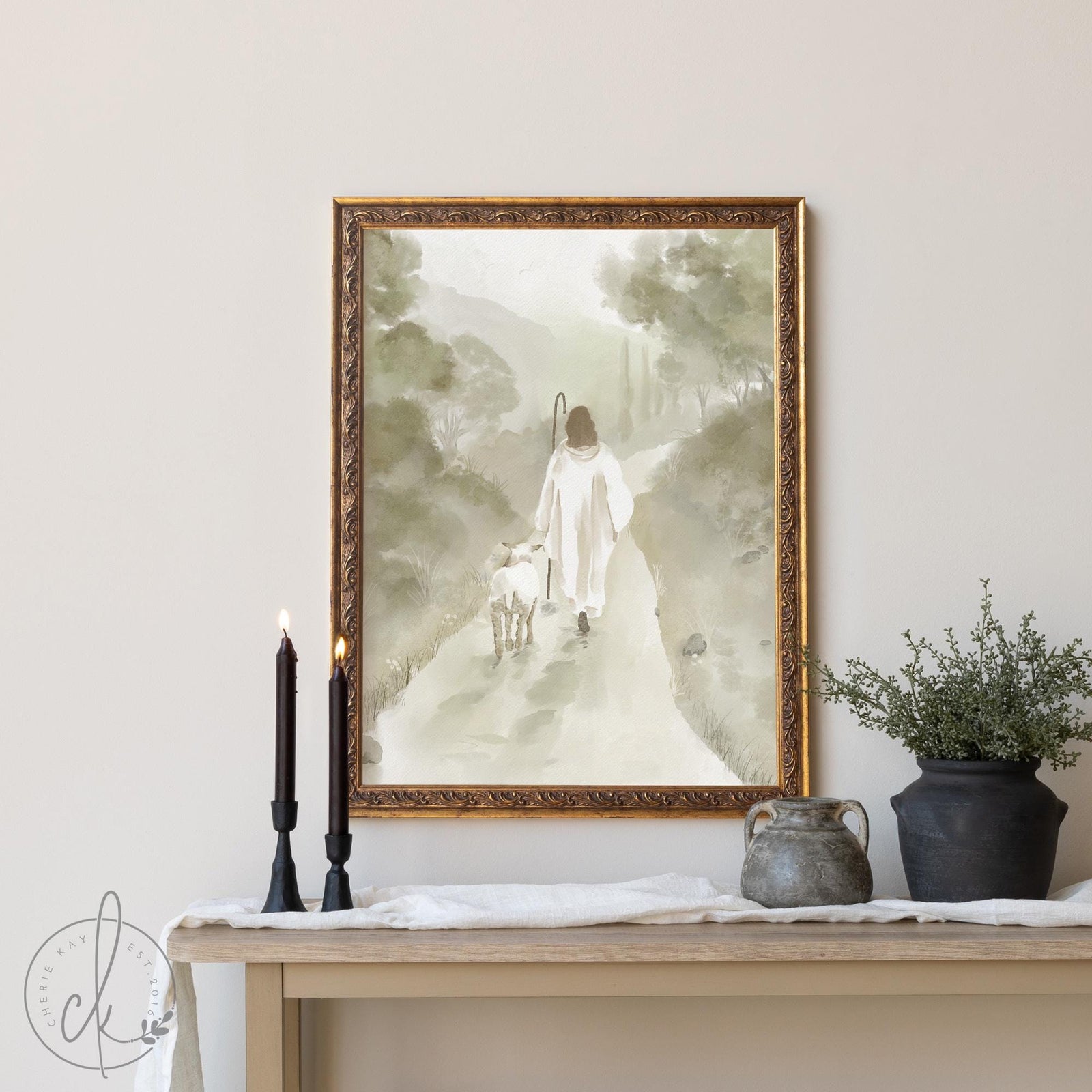 Vintage framed Jesus art showing The Good Shepherd in white robes walking with a lamb through a misty mountain landscape, rendered in soft watercolor tones with an ornate gold frame