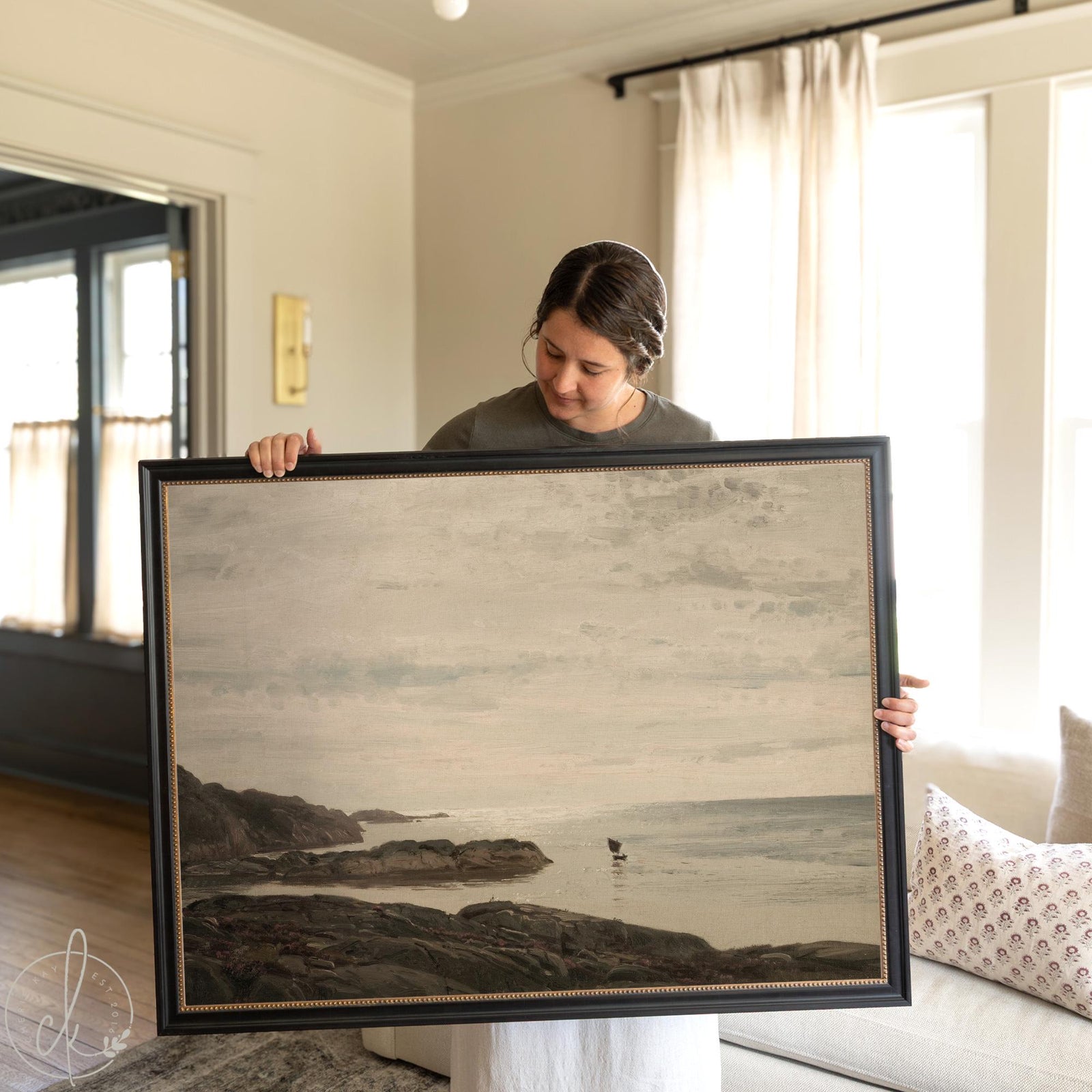 Framed coastal landscape painting of ocean and rocky shoreline in neutral colors.