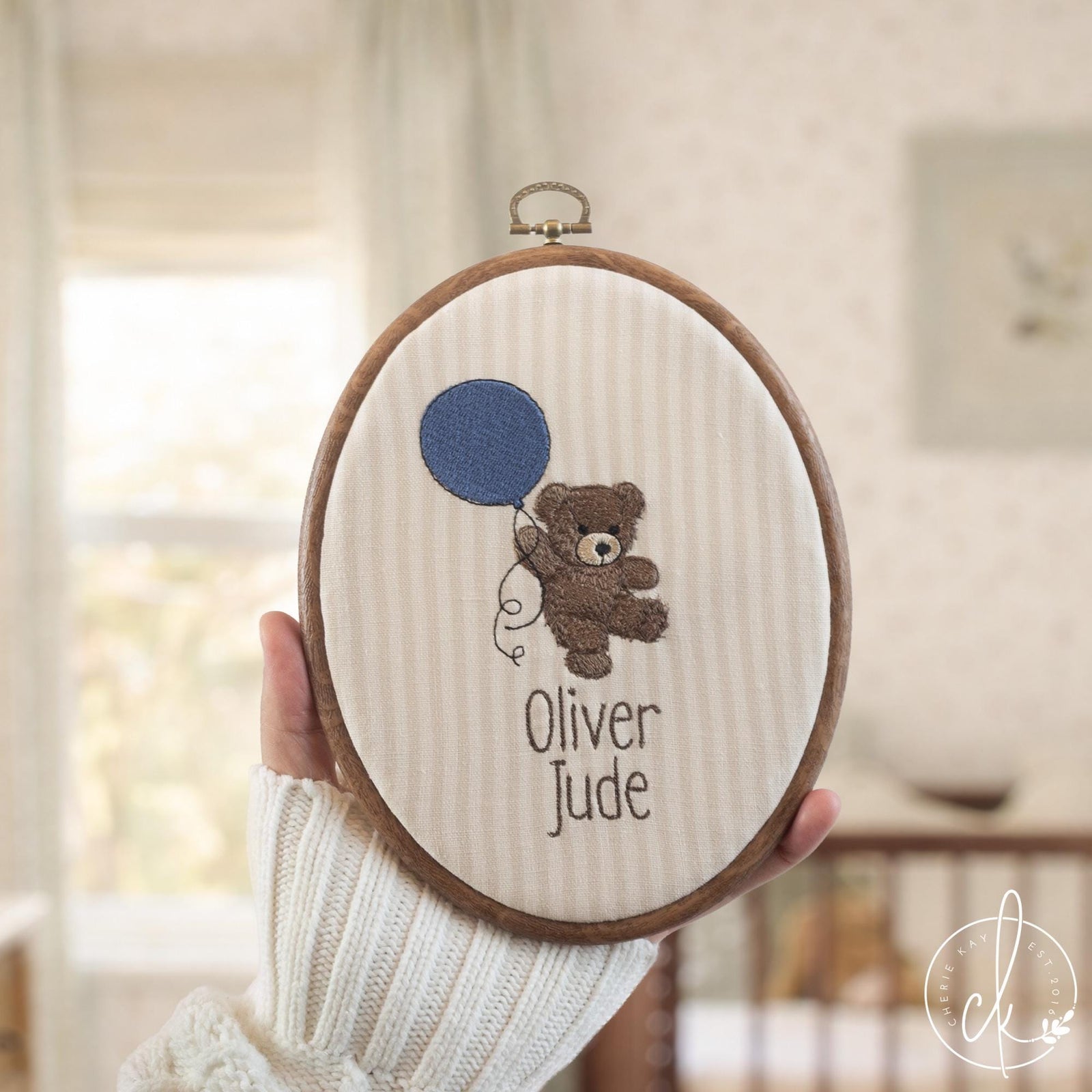 Embroidered teddy bear nursery decor with personalized baby name in oval hoop with brass hardware