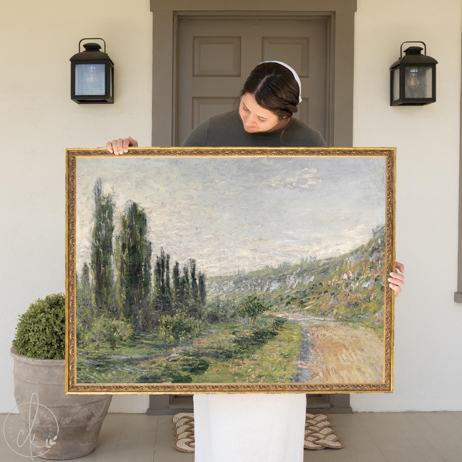 Woman holding French impressionist art framed canvas print of Monet La Route de Vetheuil landscape with poplar trees.