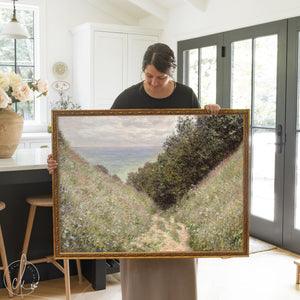 Claude Monet painting of Road at La Cavée Pourville in an ornate gold frame held inside a bright kitchen.