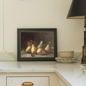 Pear still life framed canvas print in black wood frame with gold beaded trim, displayed on a kitchen counter.