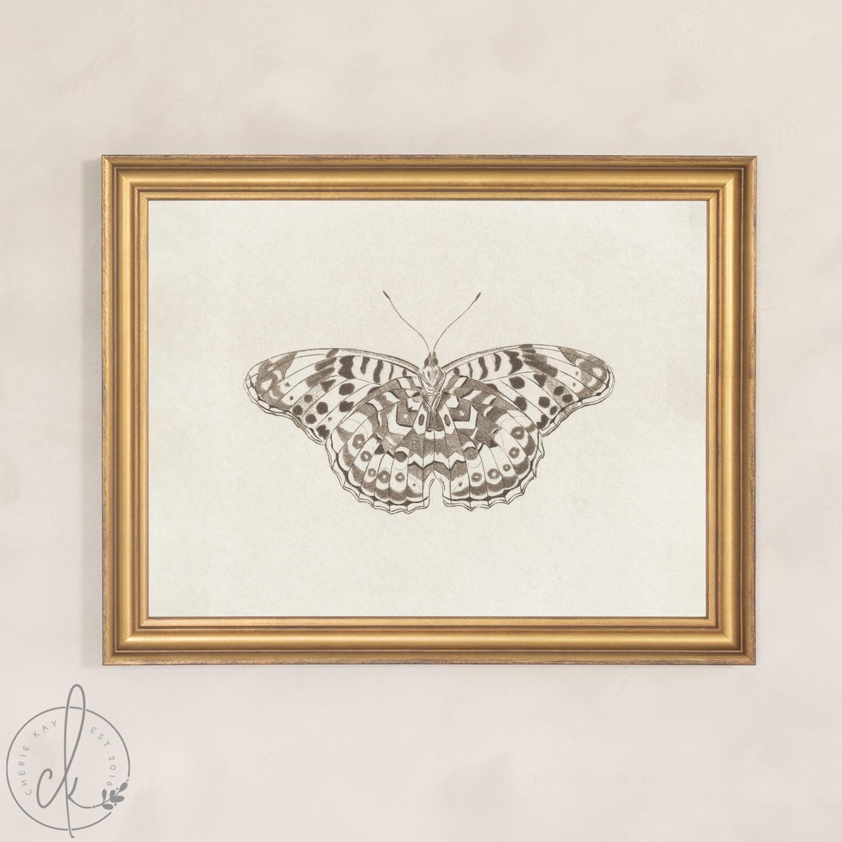 Framed butterfly art on canvas showing a single butterfly with wings spread, in a gold frame against a cream wall.