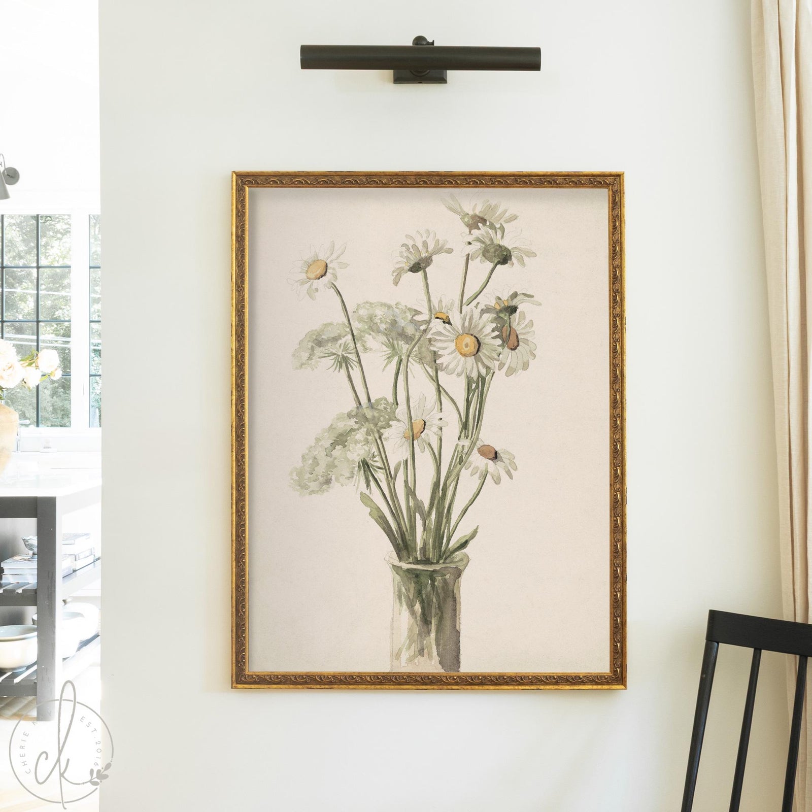 Daisy wall decor with white daisies and Queen Anne's lace in a glass vase in an ornate gold wood frame on a cream wall.