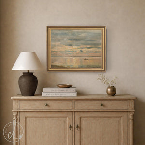 Beach sunset art with soft pastel sky and small boat on horizon, gold frame, hung above a wood console