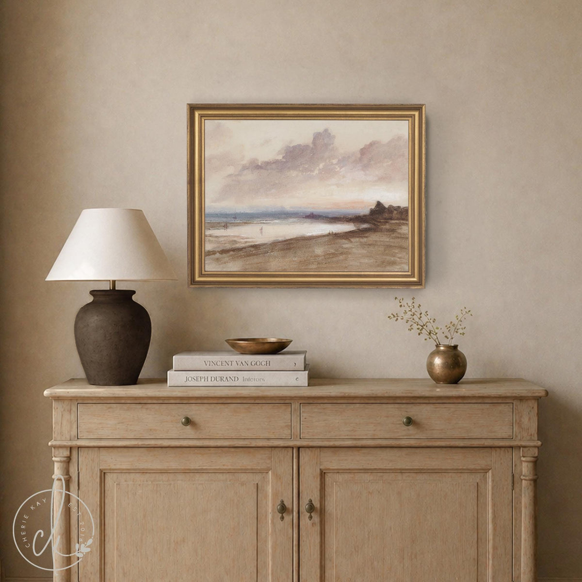 Vintage beach sunset painting in a gold frame above a wood sideboard, with mauve clouds and figures on the shore