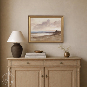 Vintage beach sunset painting in a gold frame above a wood sideboard, with mauve clouds and figures on the shore
