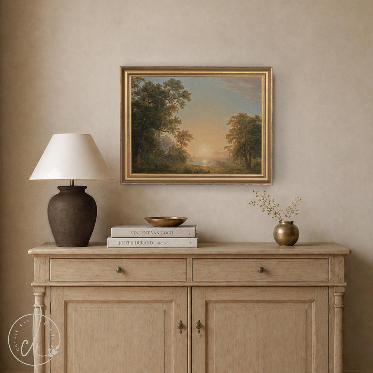 Framed sunset artwork showing a vintage style landscape with trees and a lake, in a gold frame above a wood cabinet