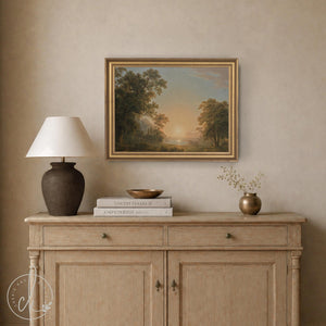 Framed sunset artwork showing a vintage style landscape with trees and a lake, in a gold frame above a wood cabinet