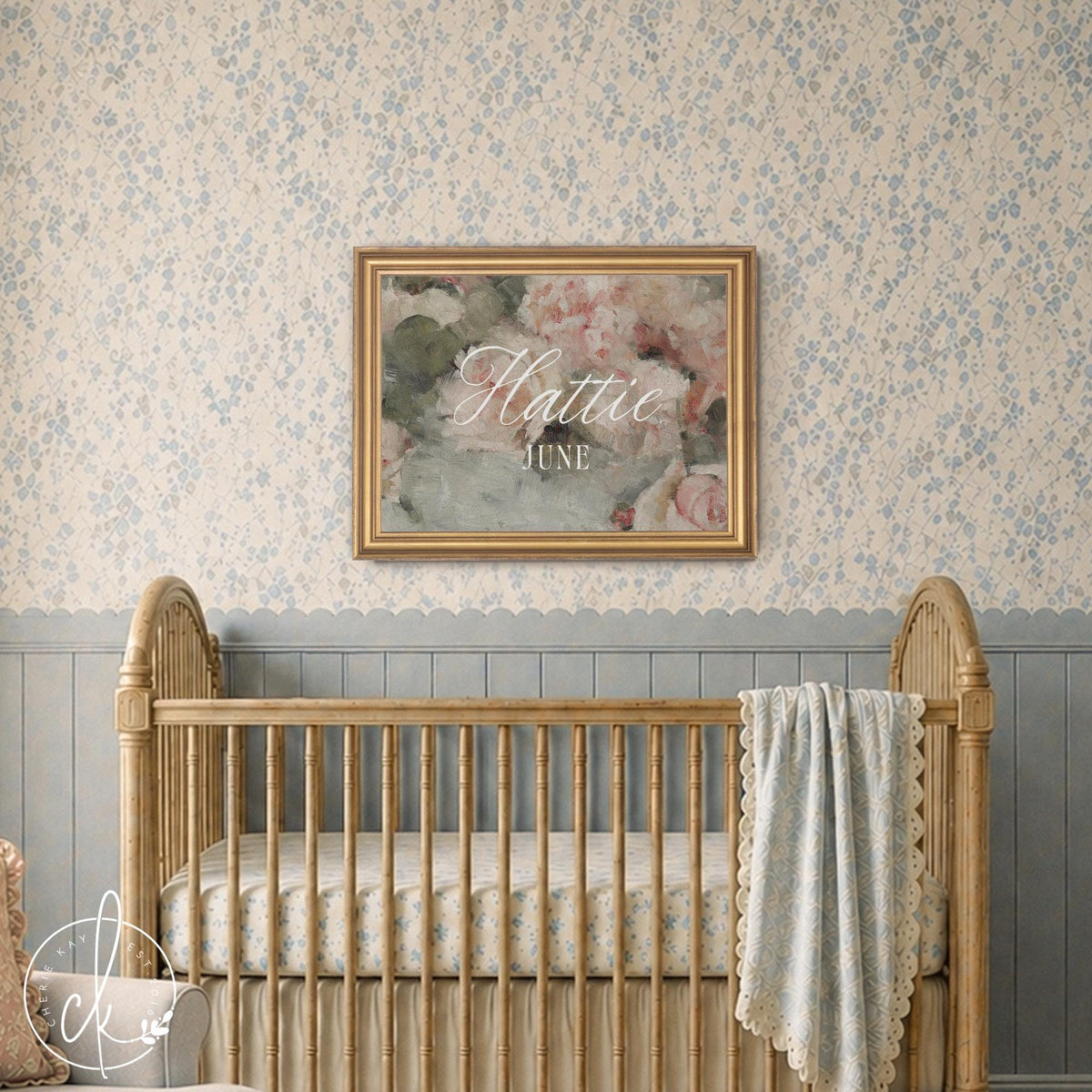 Flower nursery decor with the name Hattie June in white script on a pink peony canvas in an ornate gold frame above a crib.