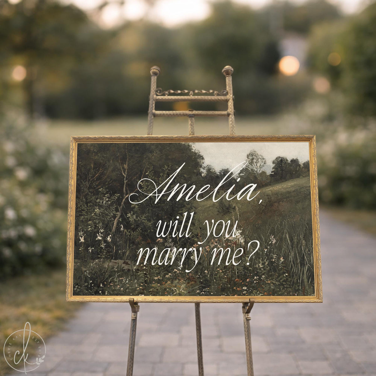 Marriage proposal sign on a brass easel, gold framed canvas reading Amelia will you marry me over a green vintage landscape