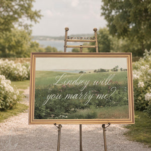 Will you marry me decor, gold framed canvas of a green landscape with wildflowers and a name in white script.