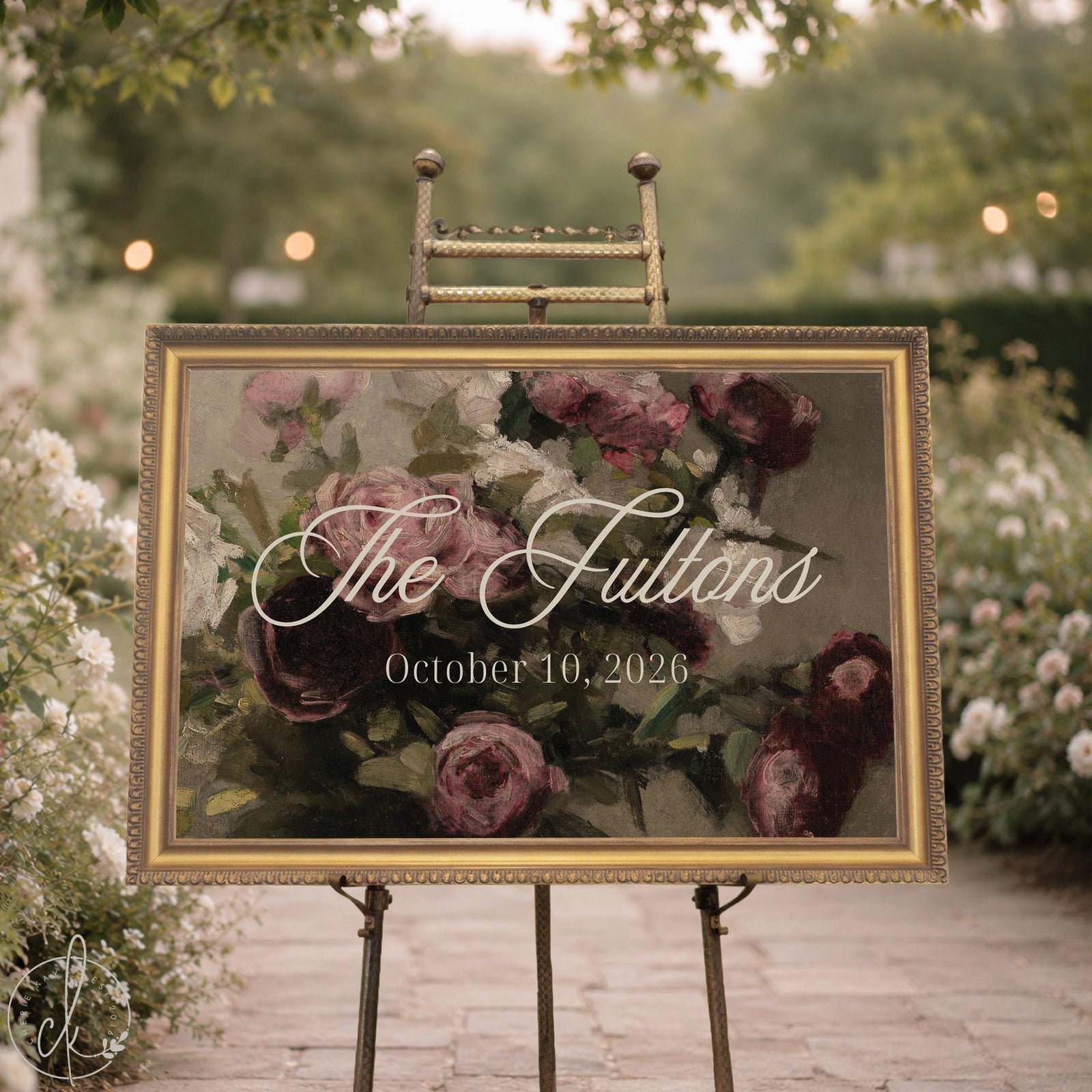 Wedding ceremony sign with last name and date over a vintage rose painting, ornate gold frame, shown on an easel in a garden.