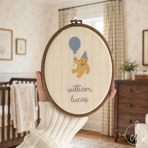 Winnie the Pooh nursery decor hoop with a gold bear holding a blue balloon above a custom name in brown script