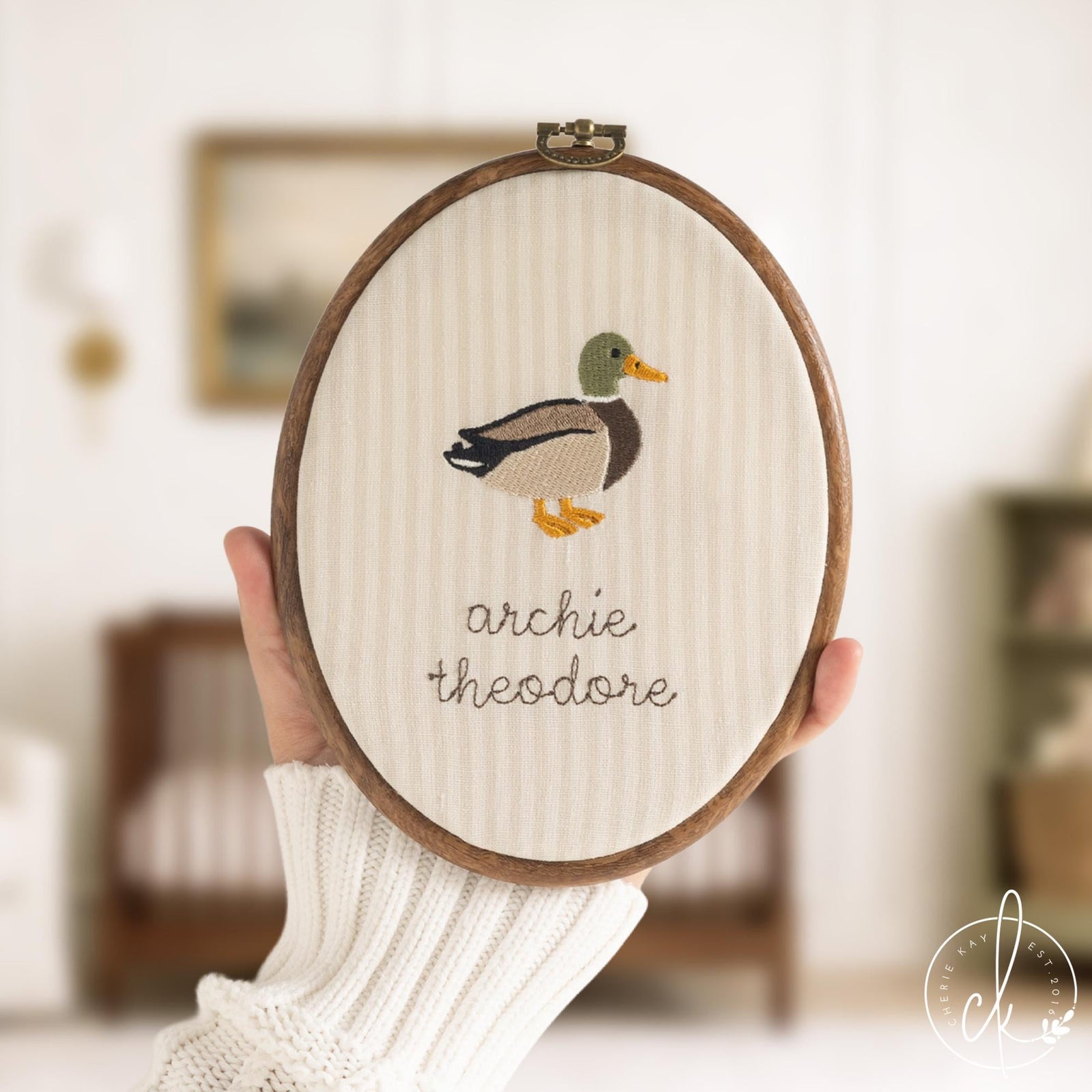 Duck nursery decor hoop with a mallard drake embroidered above a custom name in brown script on cream fabric