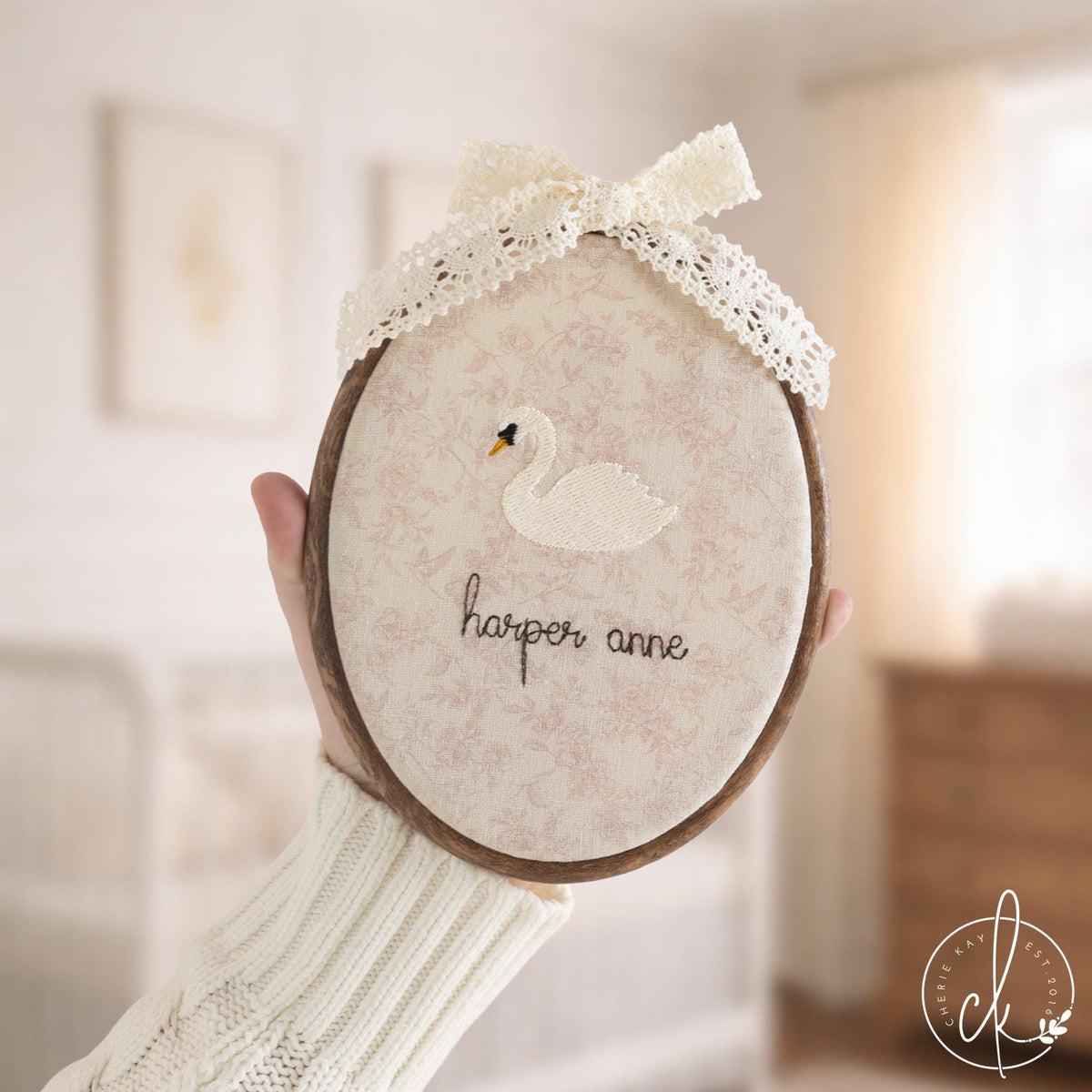 Swan nursery decor embroidery hoops with baby names in cursive on floral and striped fabric, two with cream lace bows
