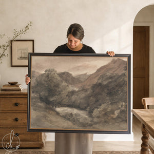 Dark landscape painting of a river valley and mountains in a black and gold frame, held up in a neutral living room