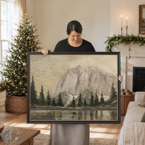 Mountain artwork in a black ornate frame, granite peak above evergreens and a still lake, hung in a living room