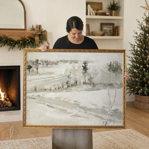 Country Christmas decor snowy hillside landscape canvas print in an ornate gold frame, held up in a living room