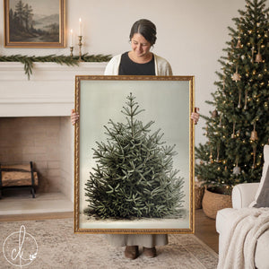 Christmas tree artwork of a snowy evergreen on a pale sage background in a gold frame, held up in a living room