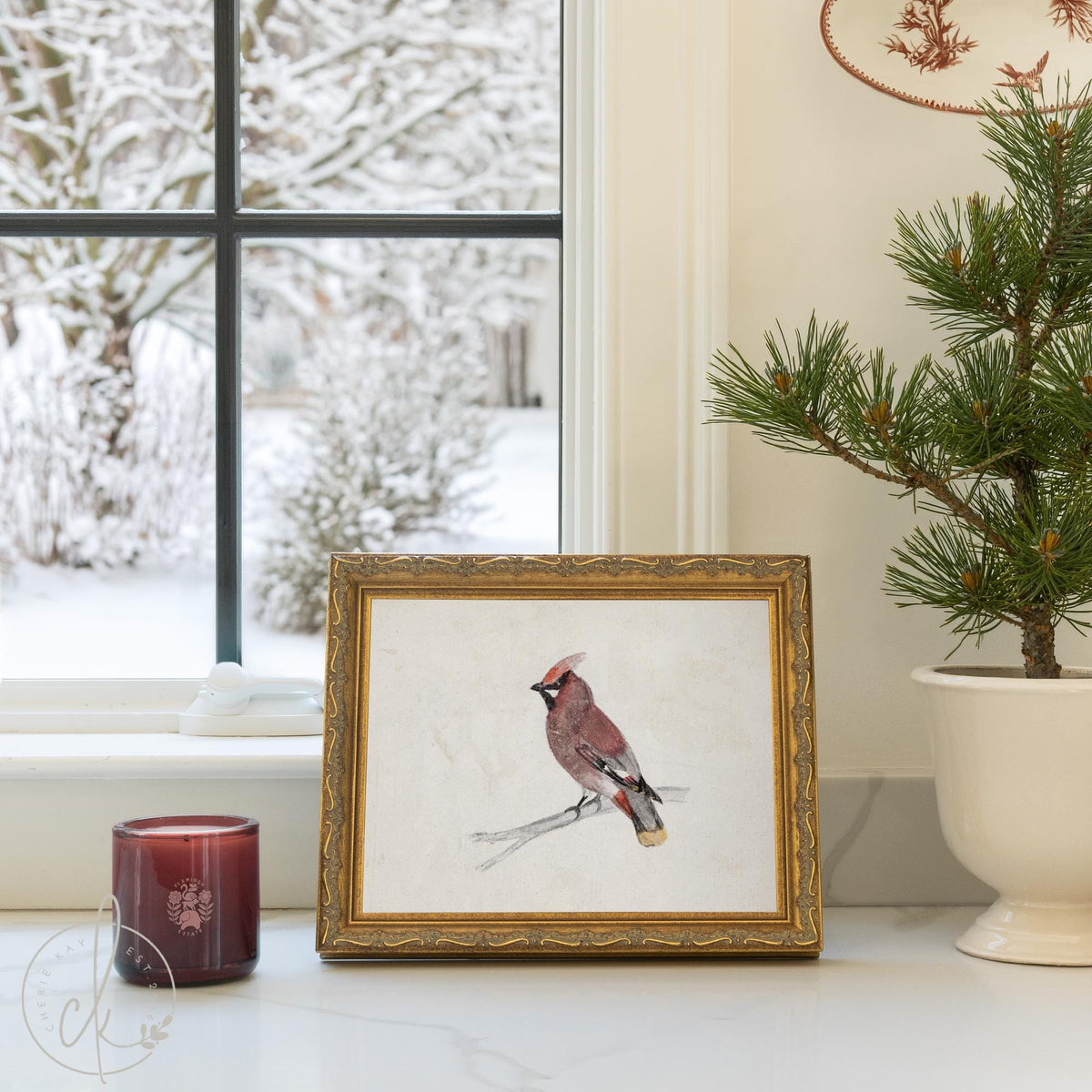 Winter bird decor showing a waxwing on a bare branch in an ornate gold frame, set on a windowsill