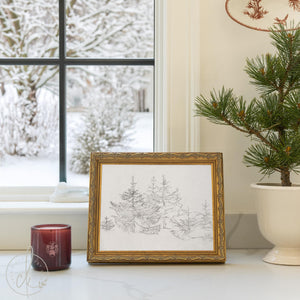Christmas tree sketch print of gray evergreens with tiny stars in an ornate gold frame, propped on a windowsill