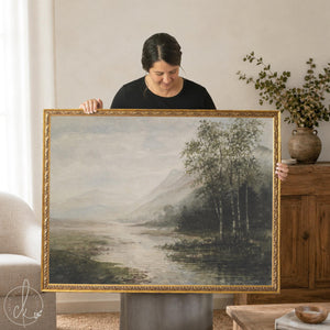Lake artwork in an ornate gold frame, misty mountains and birch trees beside a river, held up in a living room