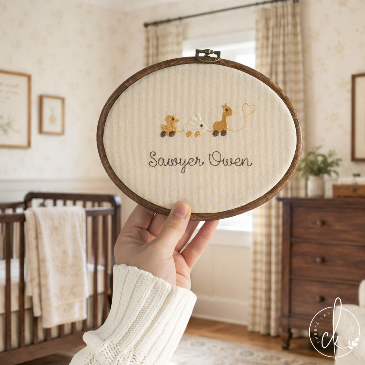 Neutral nursery decor name hoop with a duck, bunny and giraffe pull toy row on cream striped fabric, held up in a nursery
