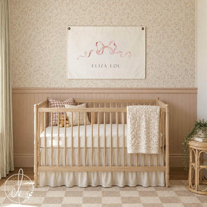Pink bow decor name canvas banner with brass grommets hanging above a wood crib in a pink nursery