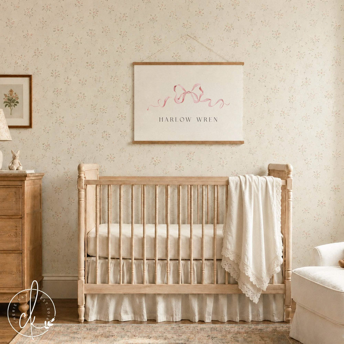 Personalized wall hanging with a pink watercolor bow and baby name on canvas, hung above a wood crib in a nursery