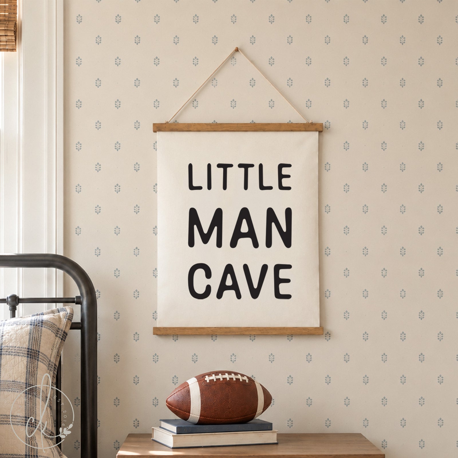 A white fabric wall hanging with the black text LITTLE MAN CAVE printed in a bold sans-serif font. The rectangular banner is held by two horizontal wooden rods at the top and bottom and is suspended by a thin white string.