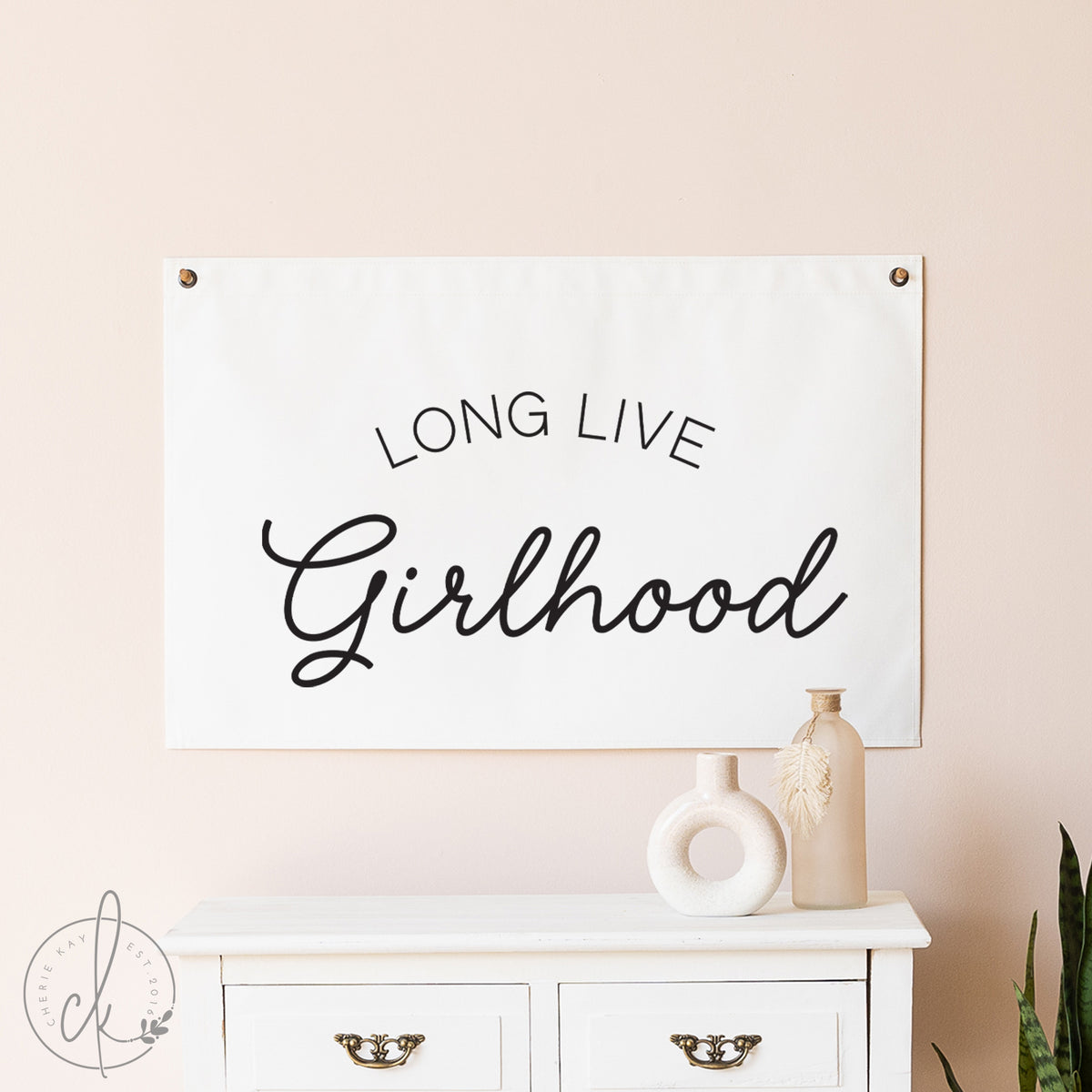 Decorative banner with 'LONG LIVE Girlhood' text on a wall above a white cabinet.
