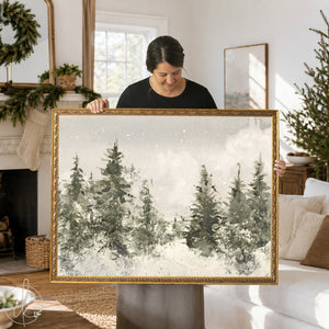 A rectangular landscape painting in a gold ornate frame featuring a watercolor-style forest scene with dark green and gray pine trees against a soft white snowy background with subtle white speckles representing falling snow.