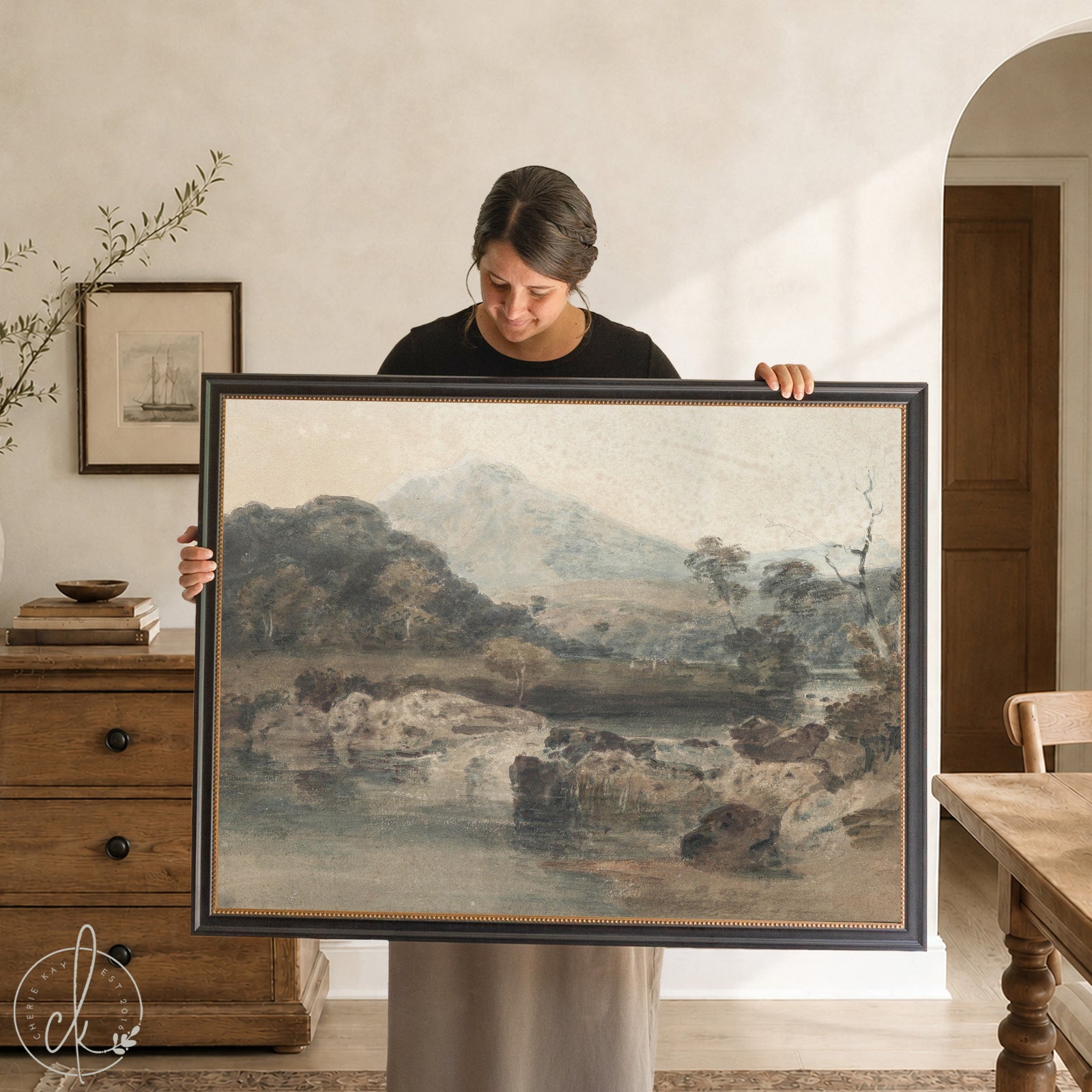Framed landscape painting on a wall above a black console table.