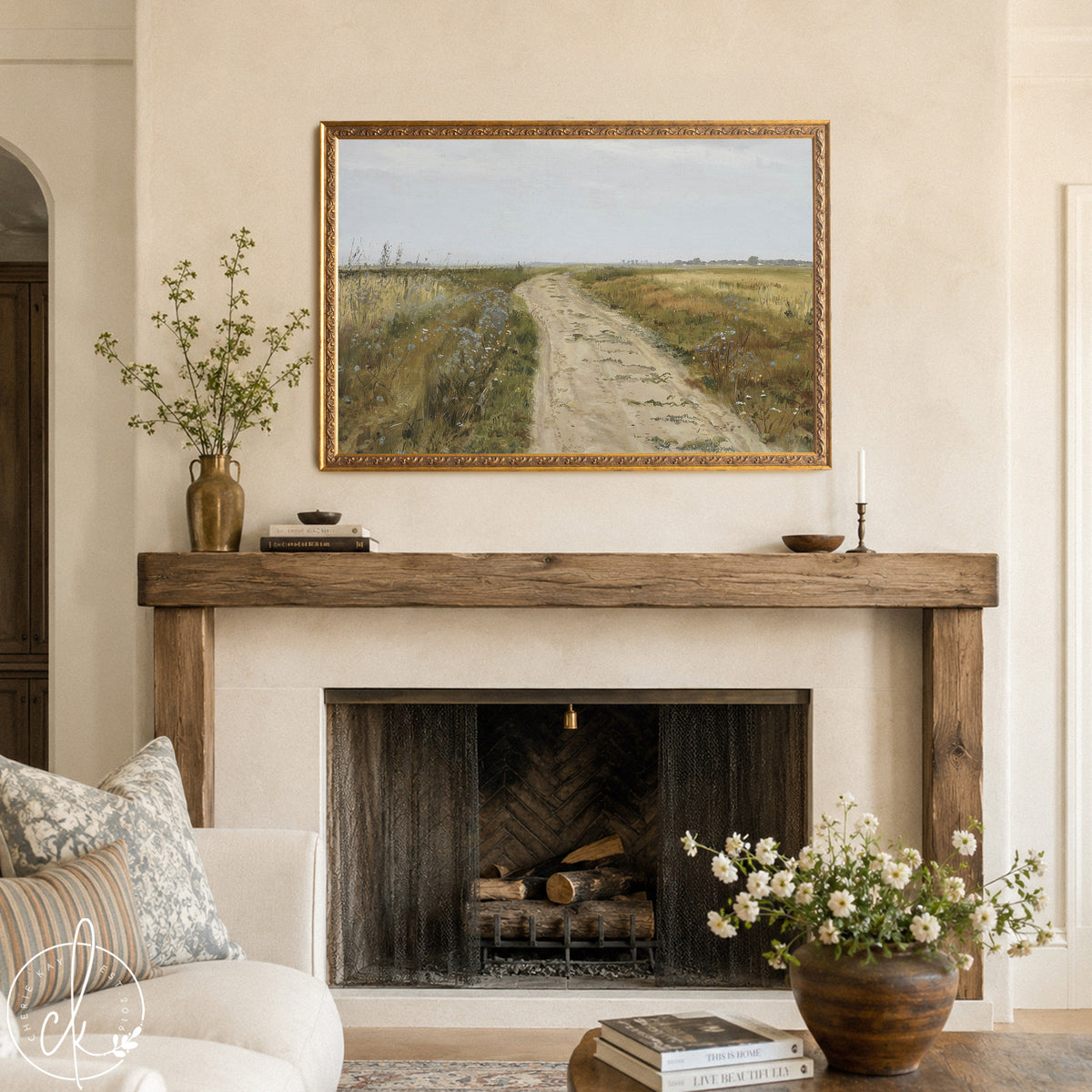 A framed landscape painting with a dirt road winding through fields of grass and wildflowers. The painting has a gold frame.