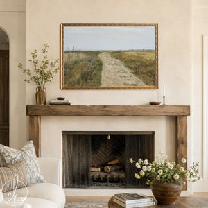 A framed landscape painting with a dirt road winding through fields of grass and wildflowers. The painting has a gold frame.