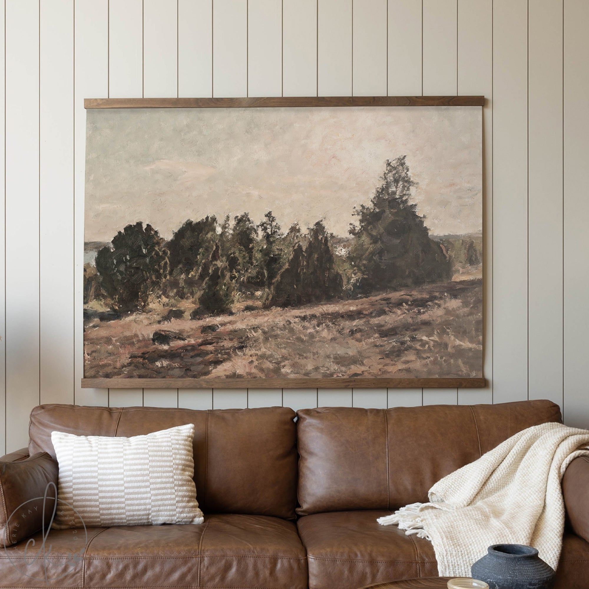 Framed landscape painting above a brown leather sofa with decorative pillows and a blanket.