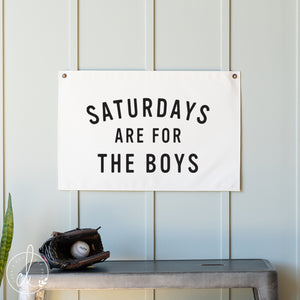 Sign with 'Saturdays are for the Boys' text on a wall with a baseball glove and ball below.
