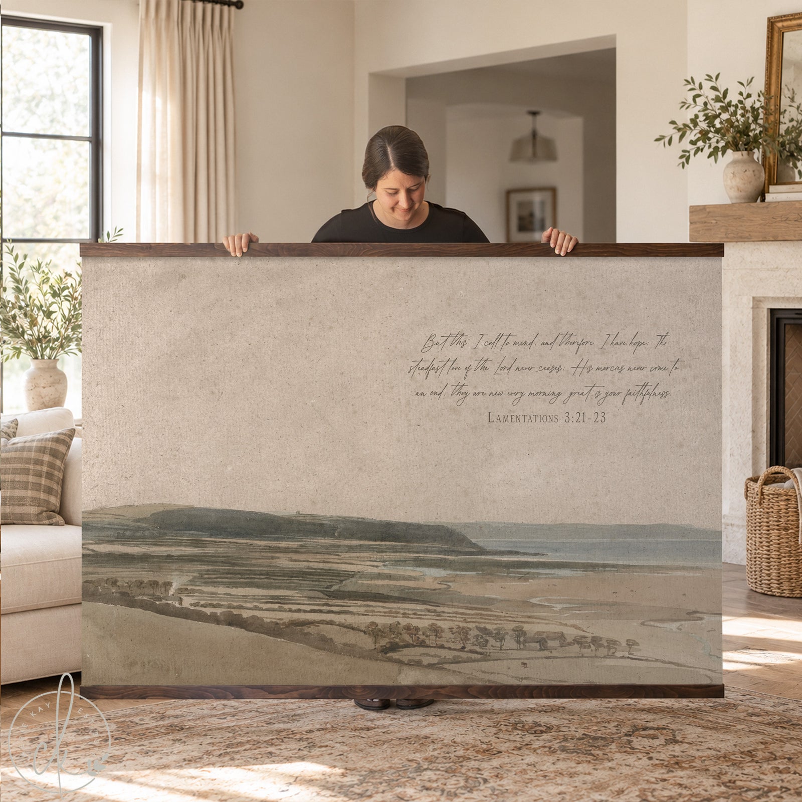 Large watercolor landscape tapestry with vintage coastal scenery and Lamentations scripture, styled above a brown leather sofa in a cozy, neutral-toned living room.